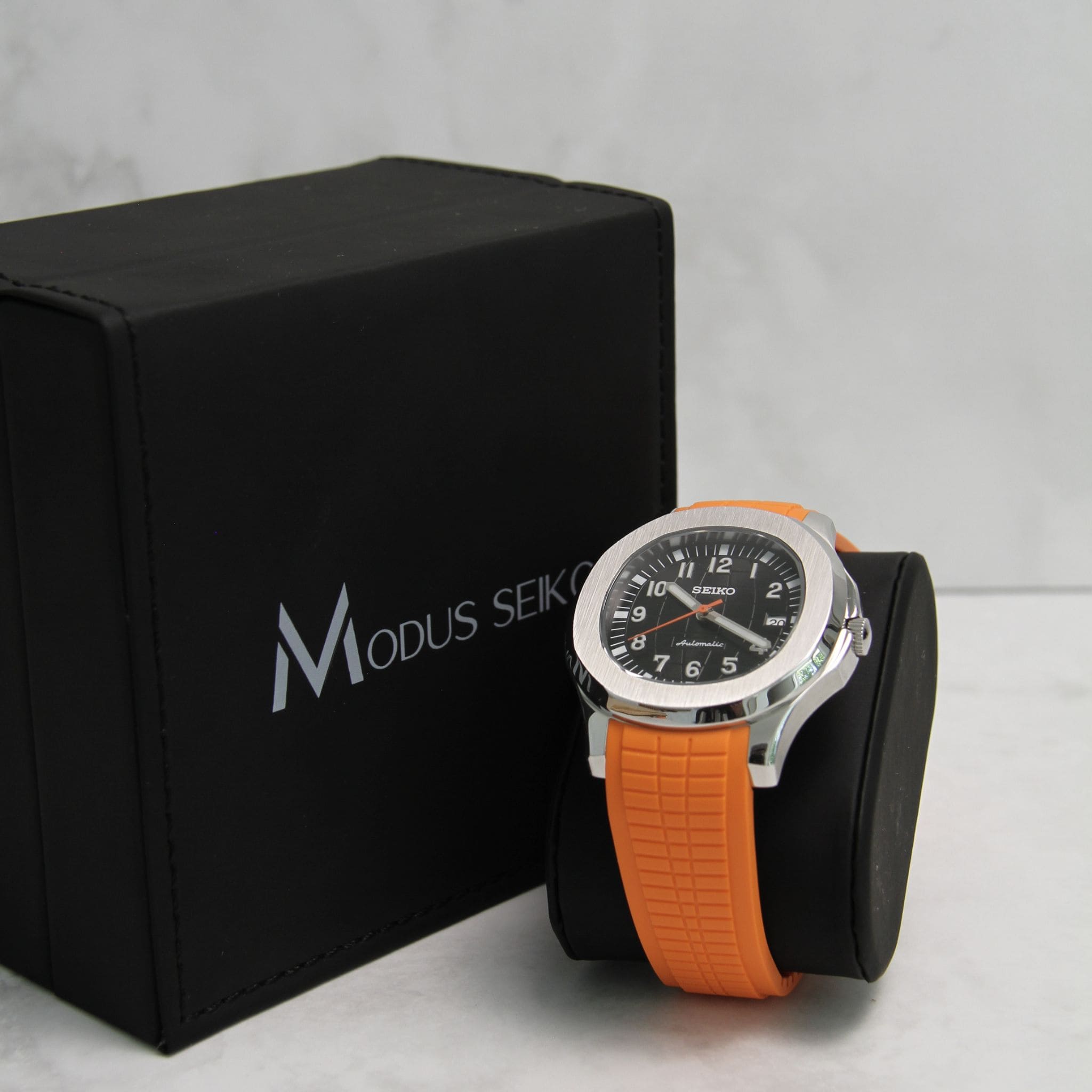 Montre Seiko Mod aquanaut orange sur coussin noir avec écrin en arrière plan.