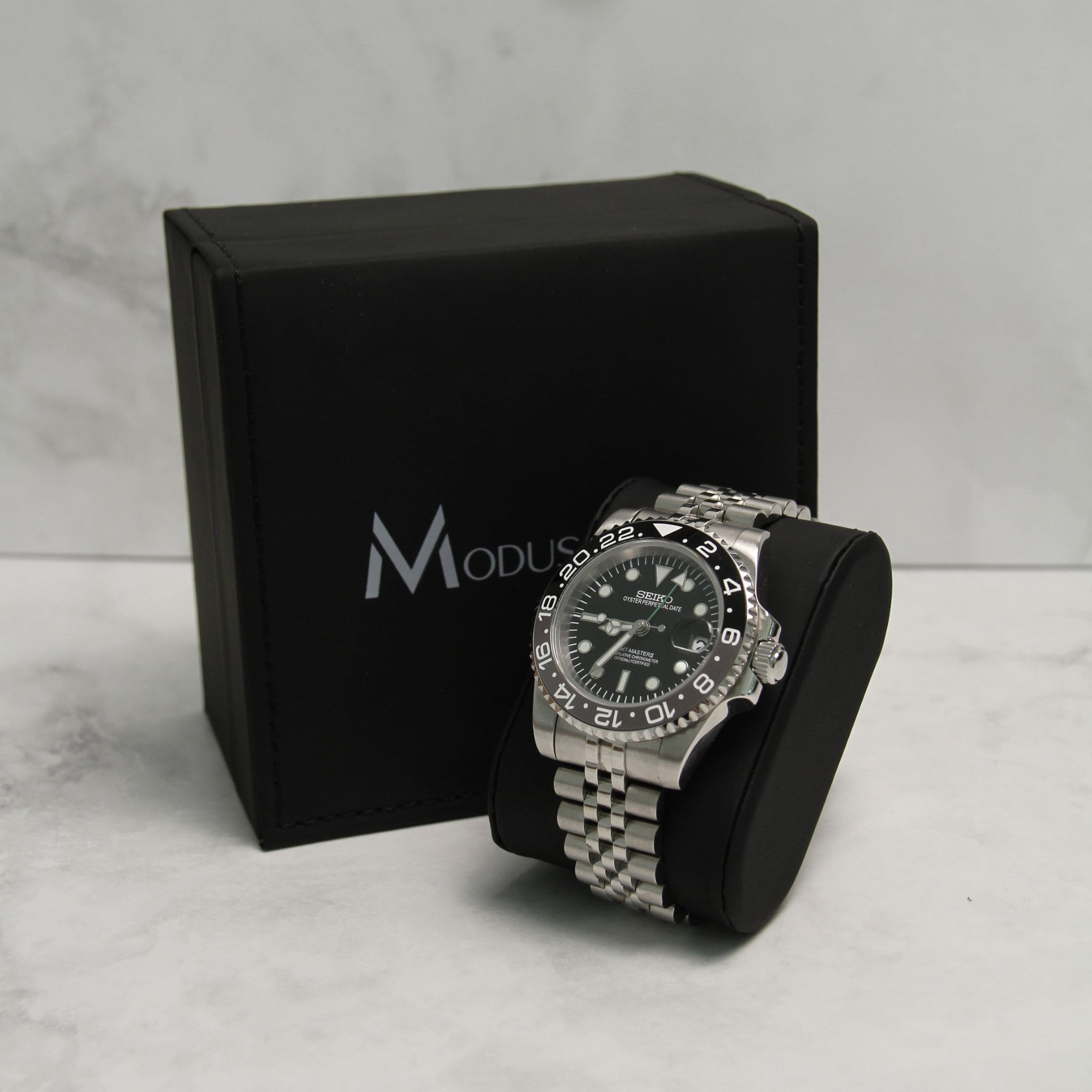 Montre Seiko Mod gmt Bruce Wayne en gros plan sur coussin noir avec écrin en arrière plan.