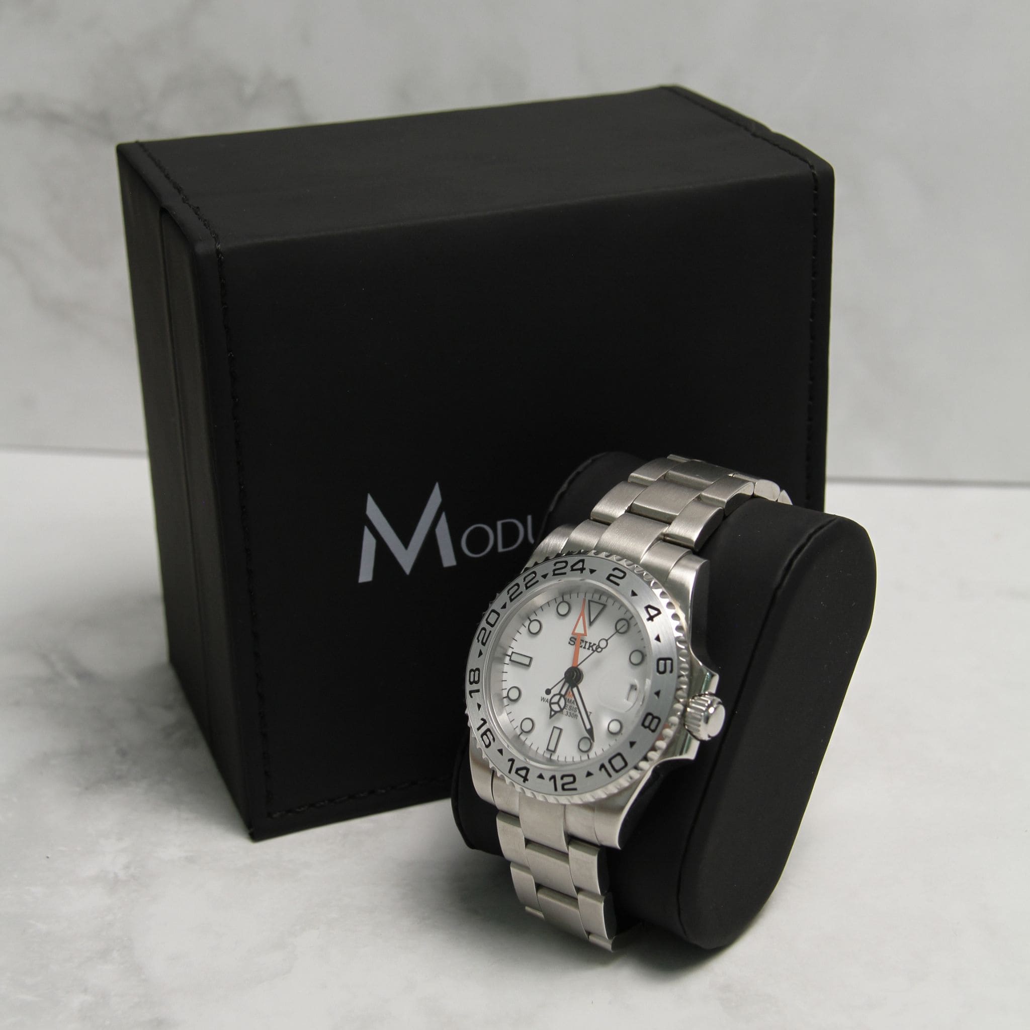 Montre Seiko Mod gmt Explorer en gros plan sur coussin noir avec écrin en arrière plan.