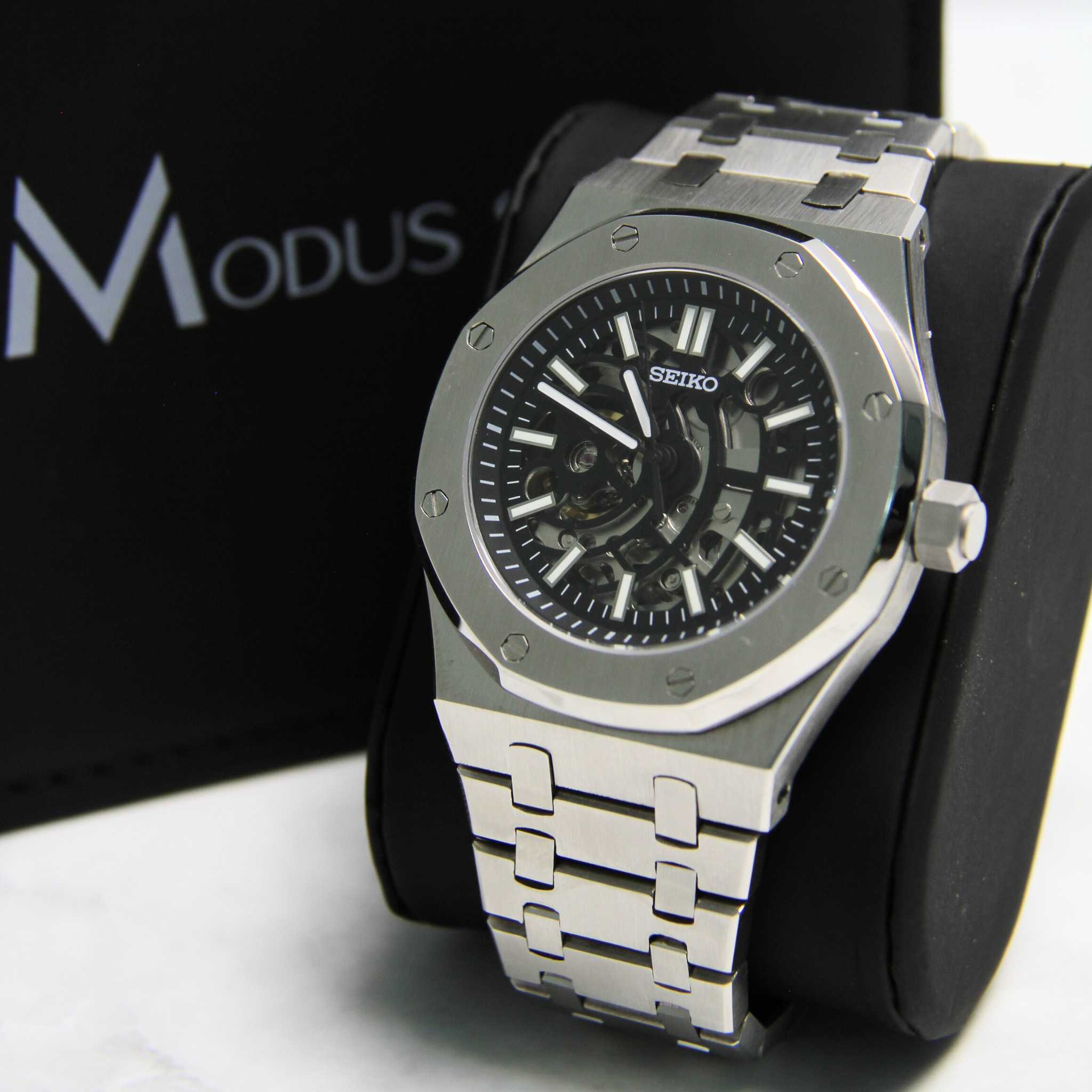 Montre Seiko Mod Royal oak squelette sur coussin noir avec écrin en arrière plan.