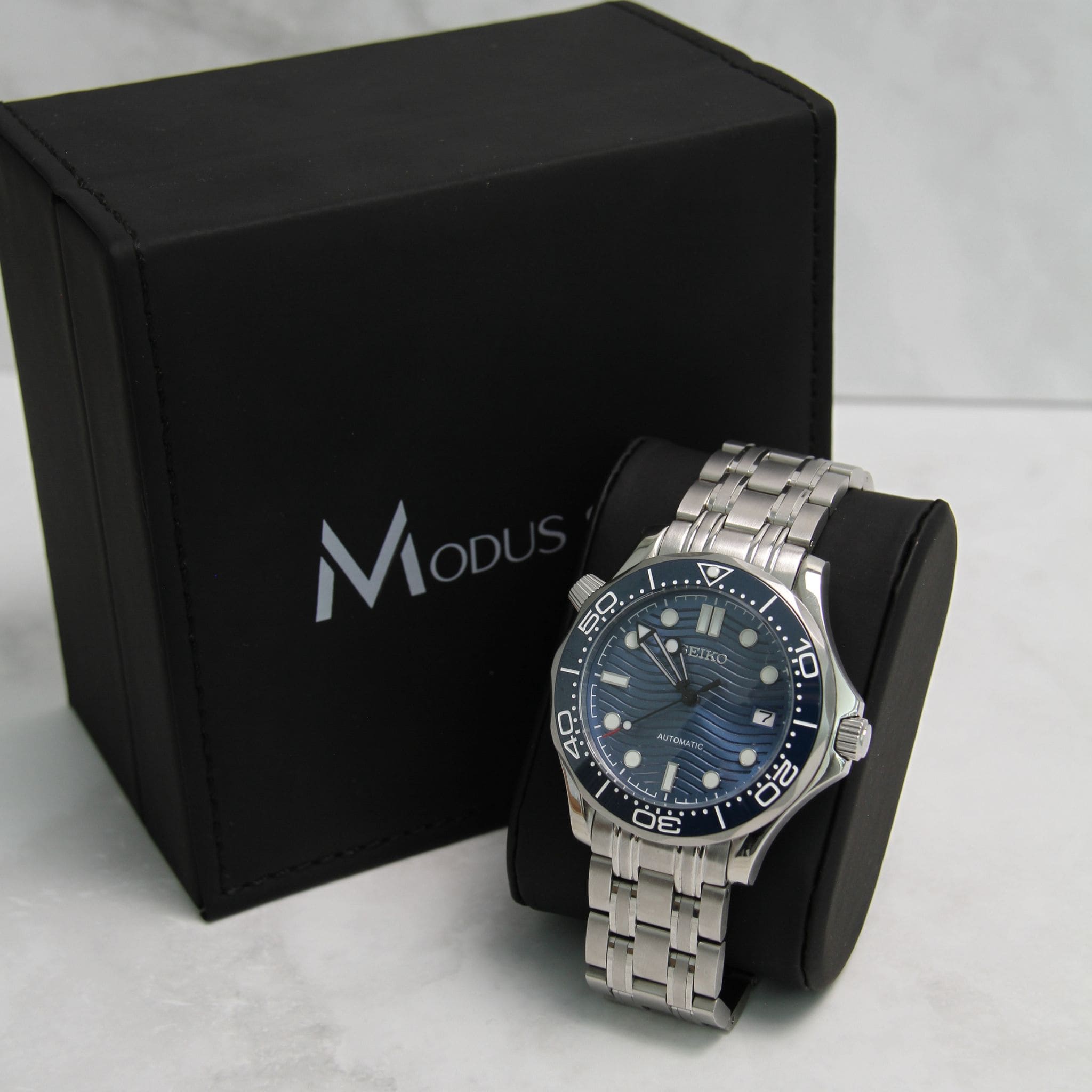 Montre Seiko Mod seamaster divers bleu sur coussin noir avec écrin en arrière plan