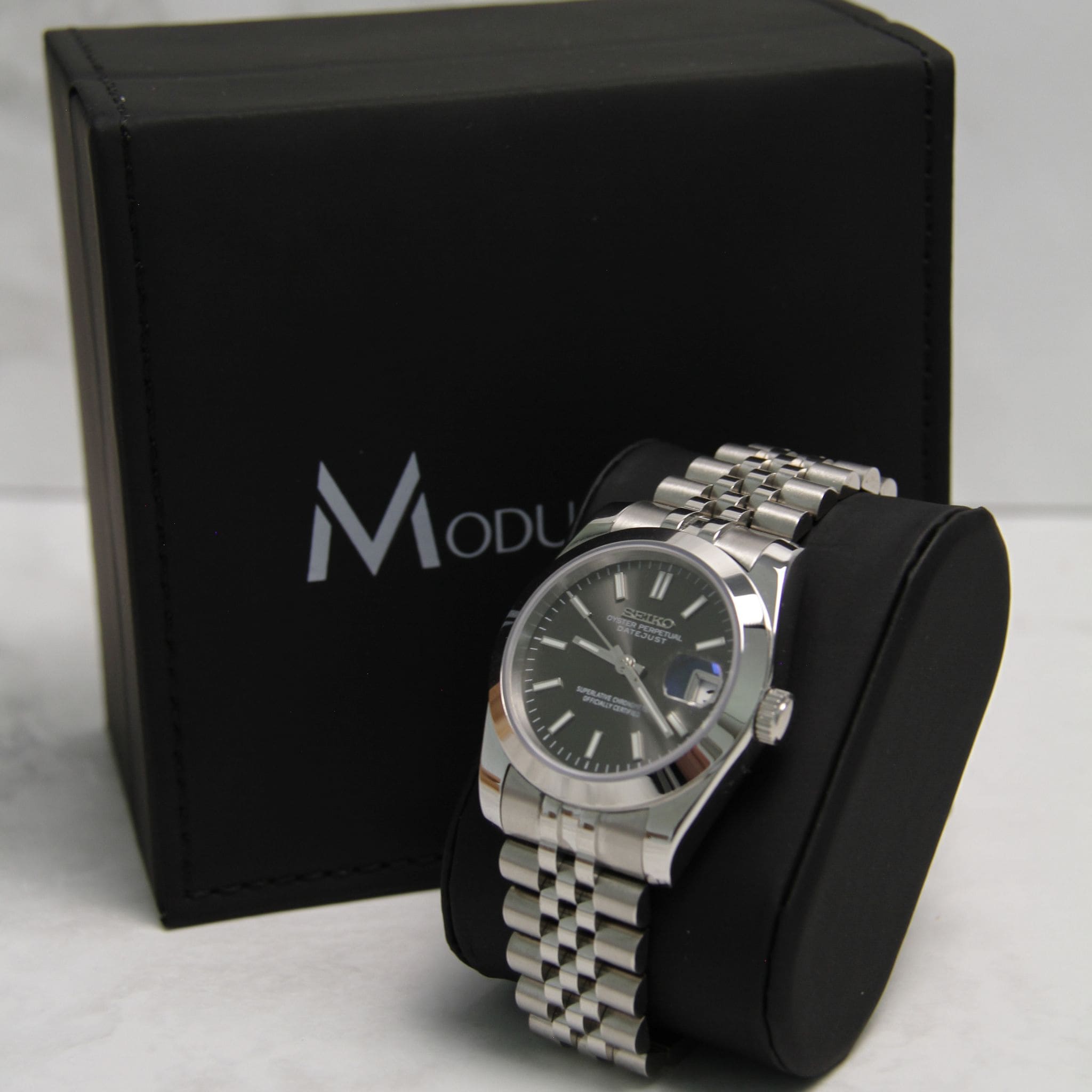 Montre Seiko Mod datejust gris 36mm sur coussin noir avec écrin en arrière plan