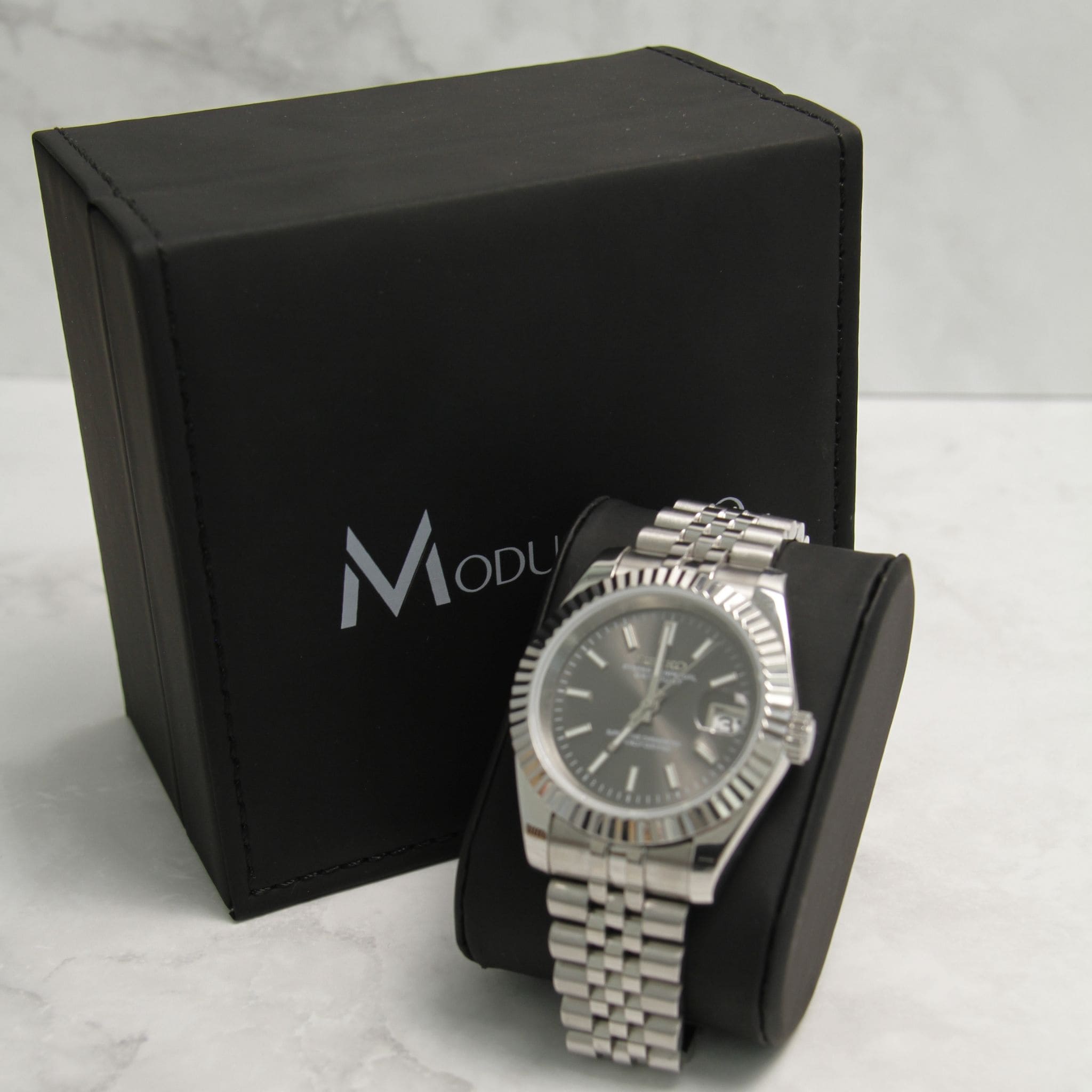 Montre Seiko Mod datejust gris sur coussin noir avec écrin en arrière plan