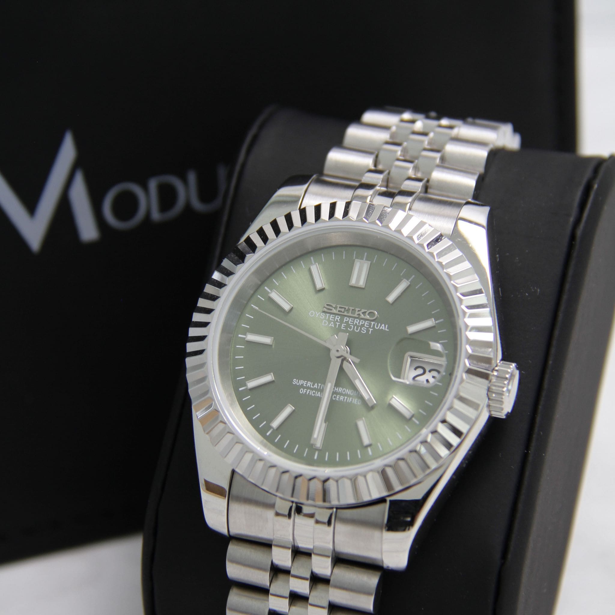 Montre Seiko Mod datejust kaki arabic sur coussin noir avec écrin en arrière plan.