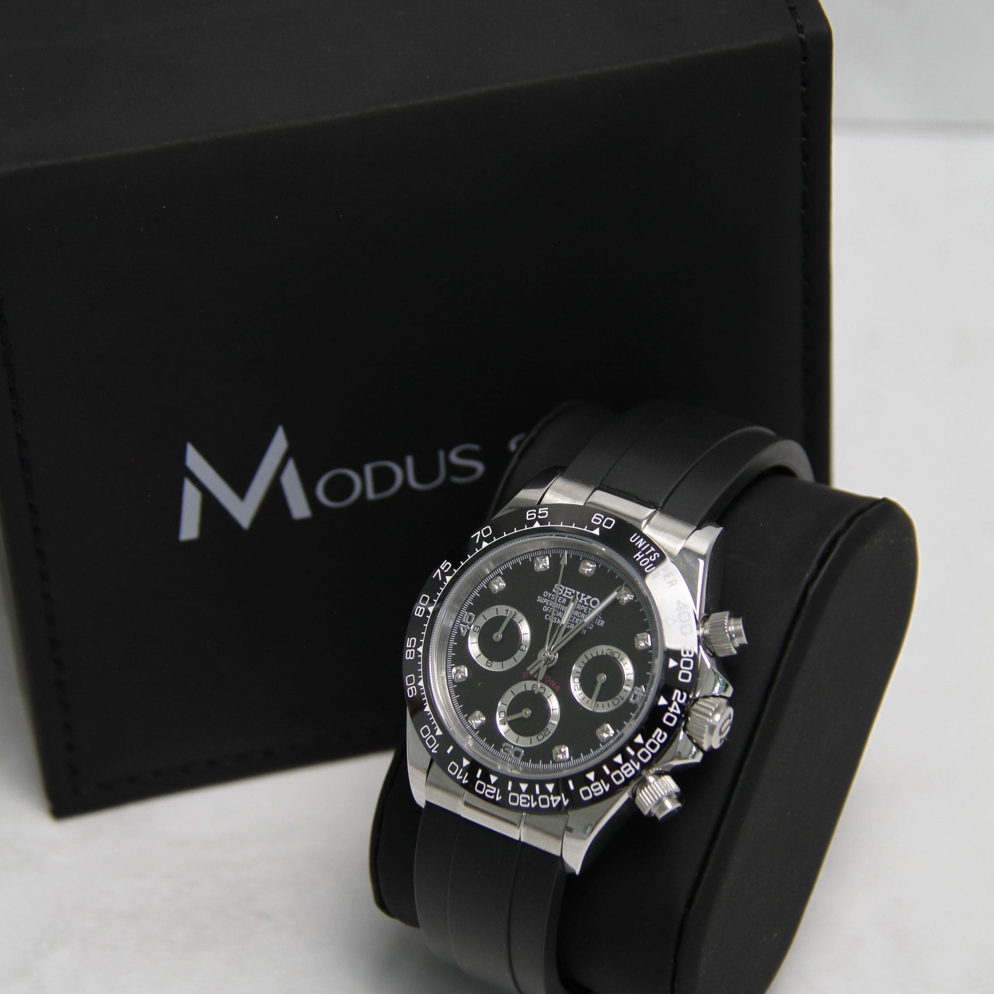 Montre Seiko Mod daytona noir argent diamant sur coussin noir avec écrin en arrière plan.