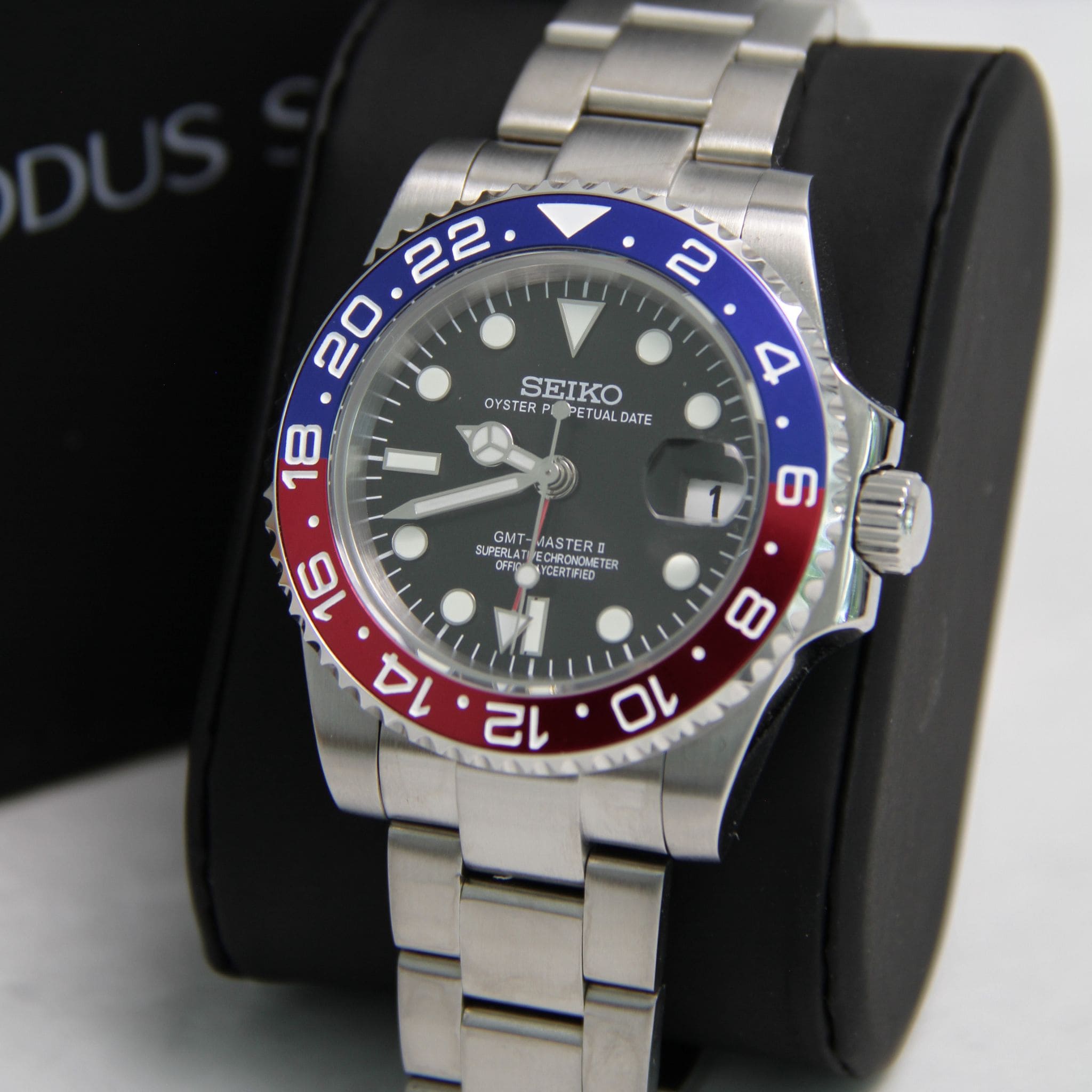 Montre Seiko Mod gmt Pepsi en gros plan sur coussin noir avec écrin en arrière plan. 